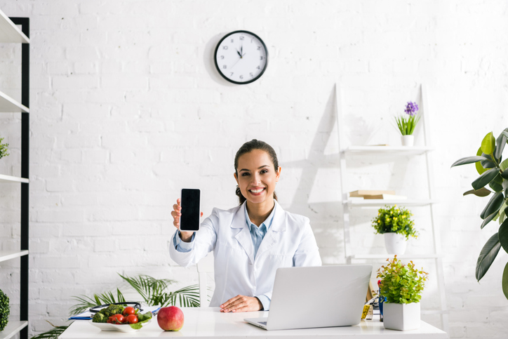 nutrition services: nutritionist holding phone out while at desk on laptop